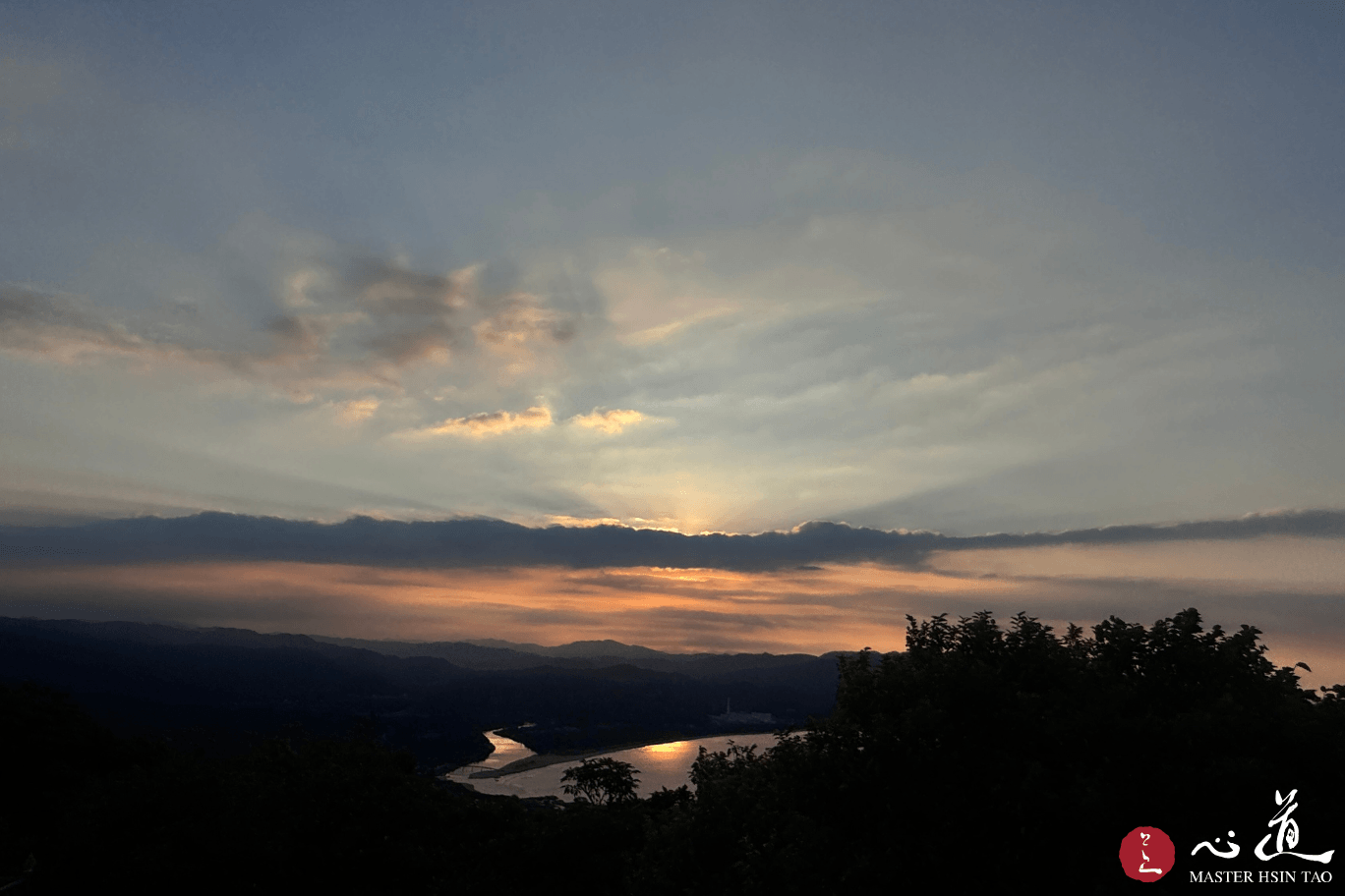 靈鷲山高處俯瞰夕照山河，霞光映照水面，象徵心道法師教導出家人以善業照亮人天、利益眾生